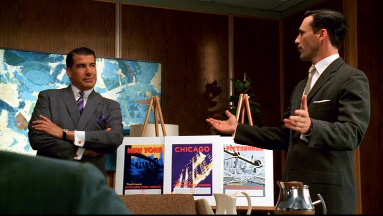 a man in suit standing in front of a table with posters