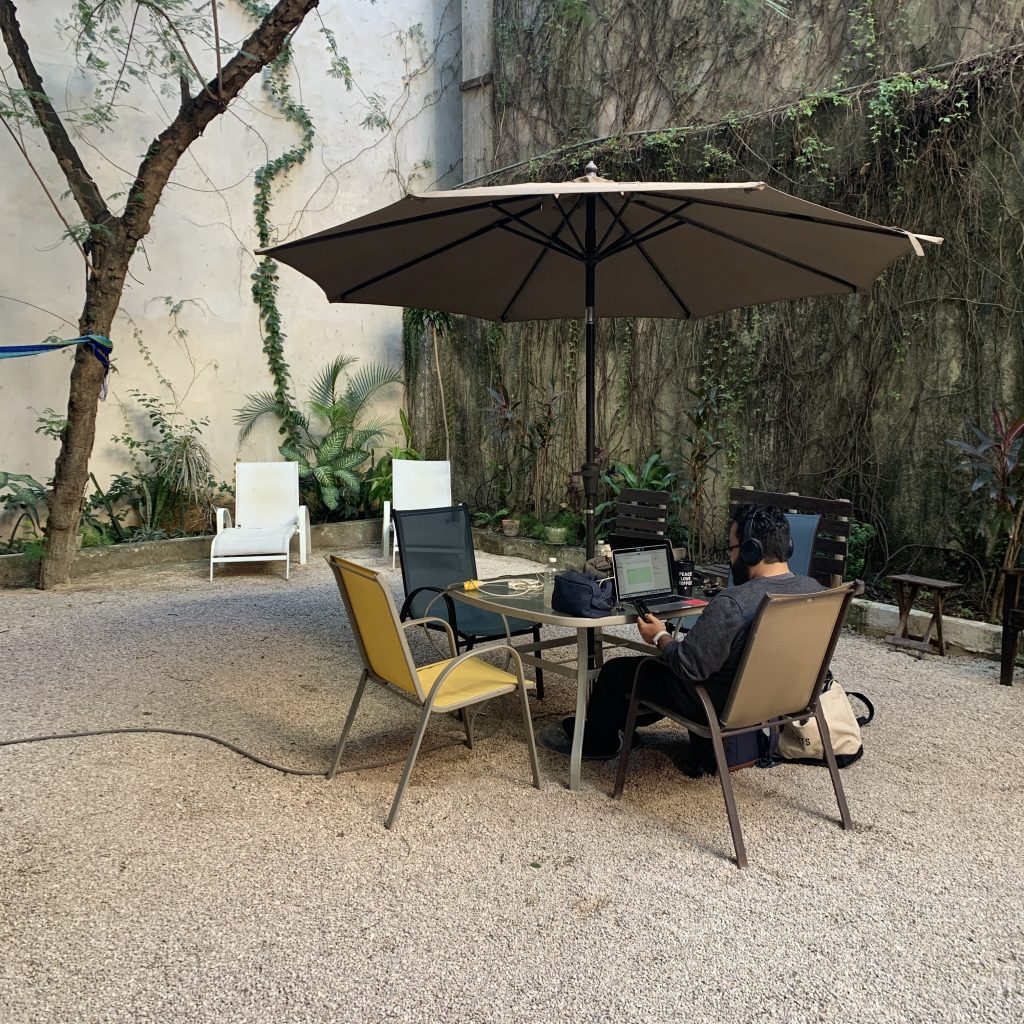 a man sitting at a table with a laptop under an umbrella