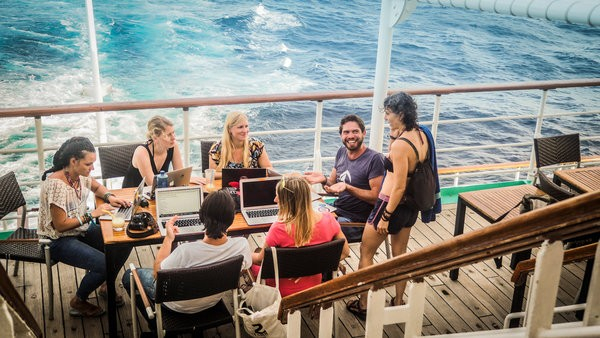 a group of people sitting at a table with laptops on a boat