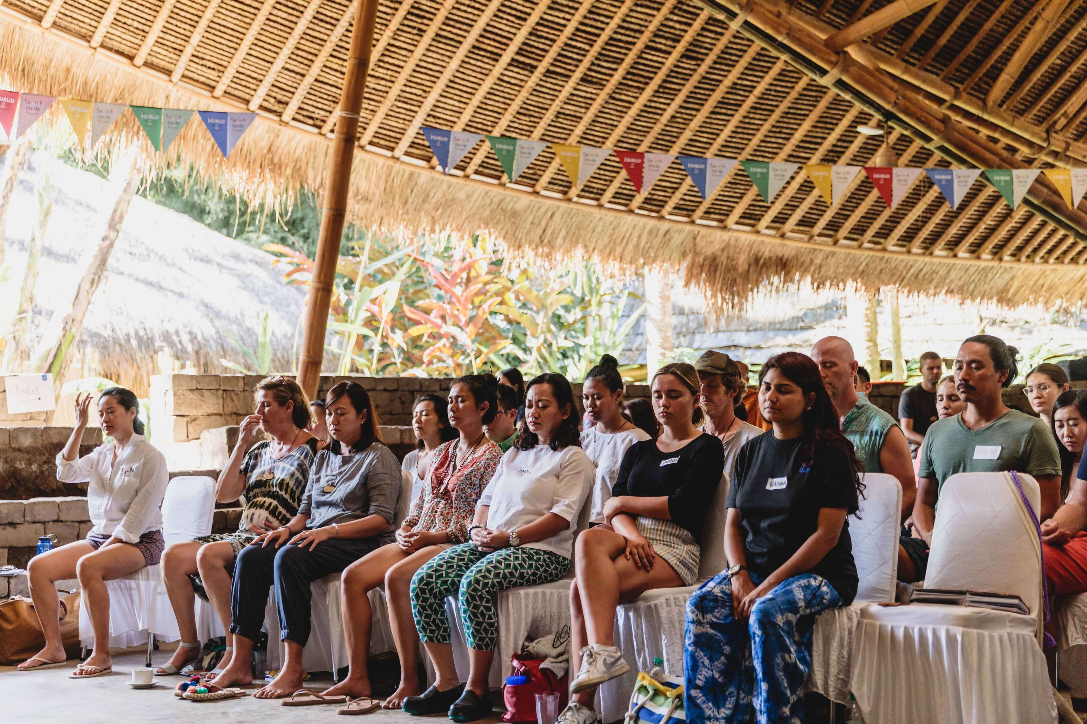 a group of people sitting on white benches under a straw roof