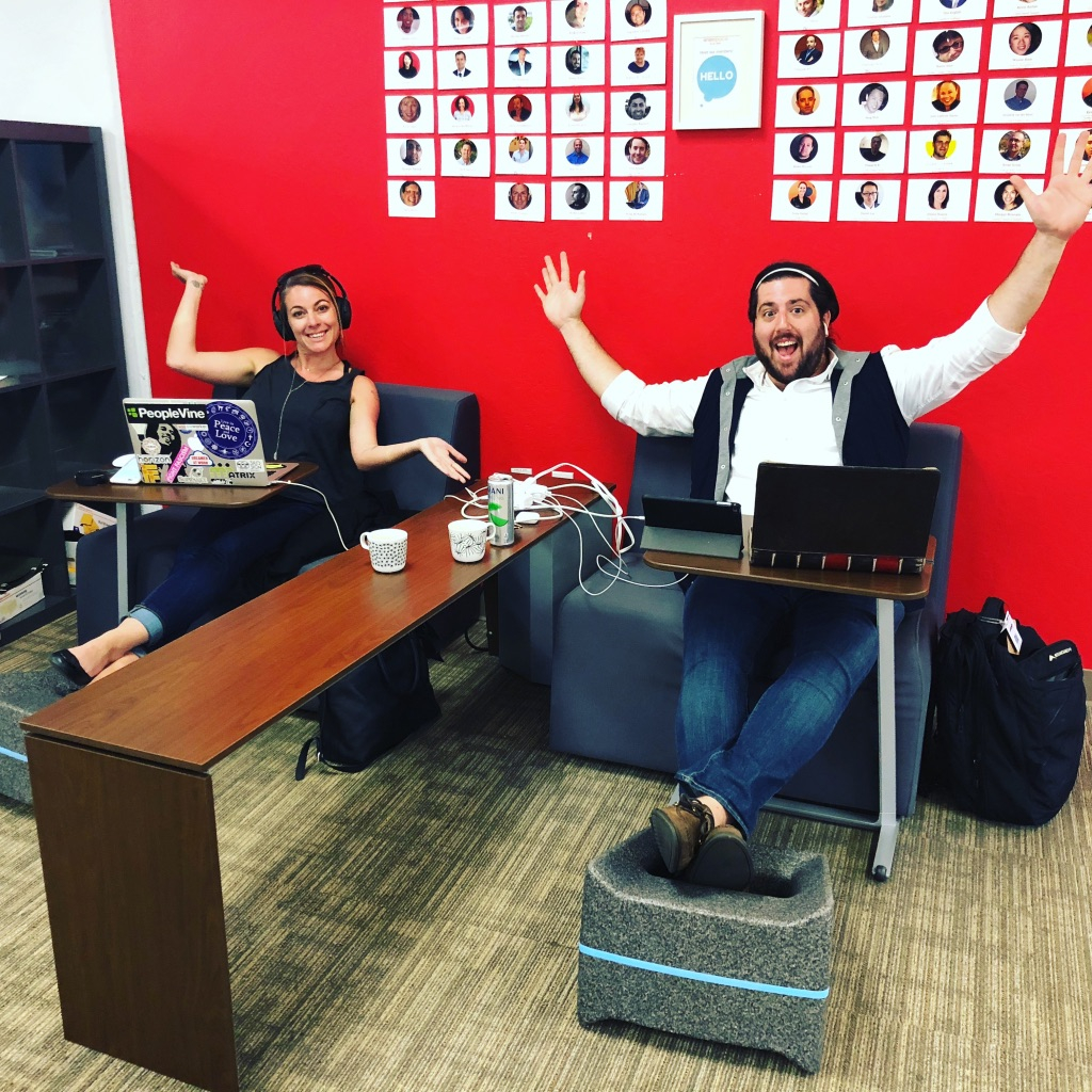 a man and woman sitting at a desk with their arms up