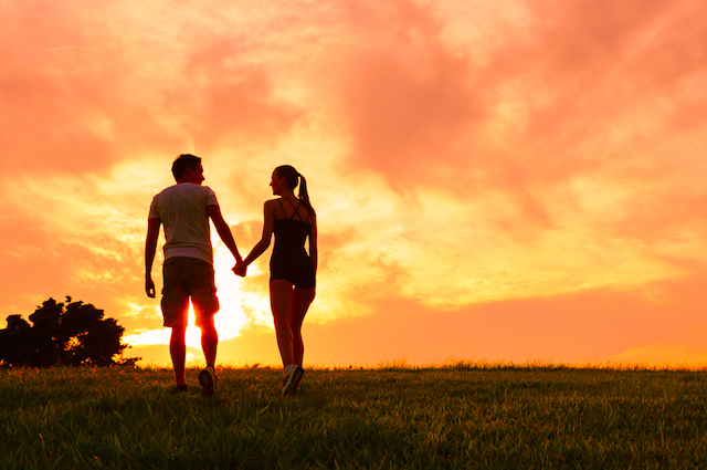 a man and woman holding hands and walking in a grassy field