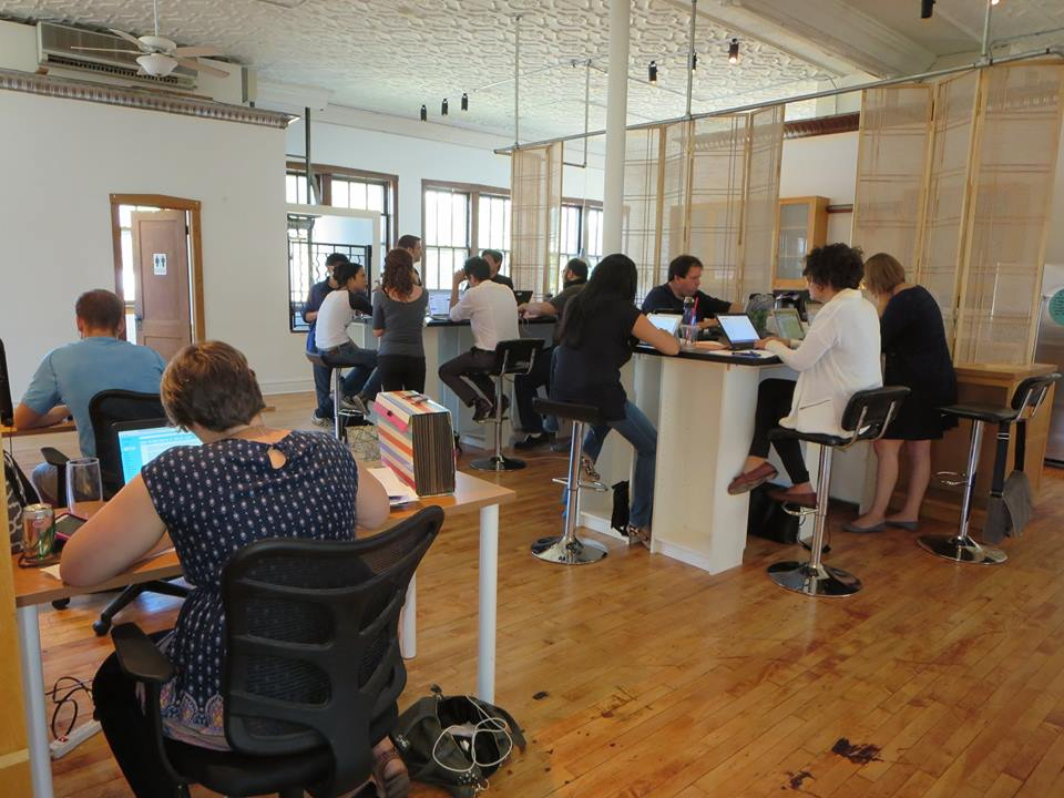 a group of people sitting at tables in a room with laptops