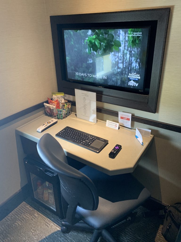 a computer on a desk with a television on the wall