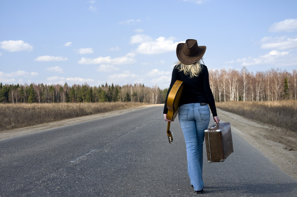 a woman walking on the road with a guitar and suitcase