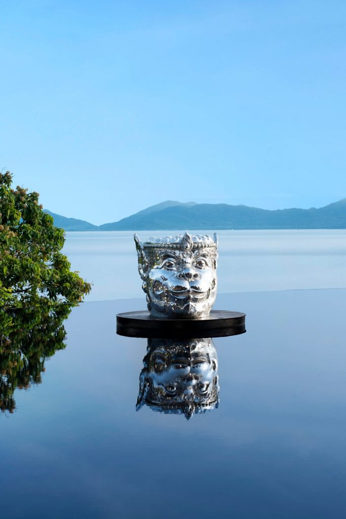 a silver cup on a black platform with a body of water and mountains in the background