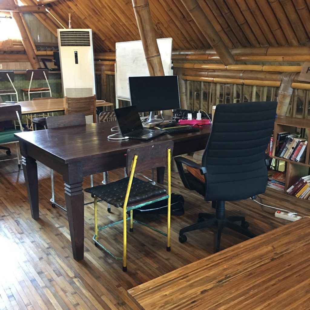 a desk with a computer and chairs in a room with a bamboo roof