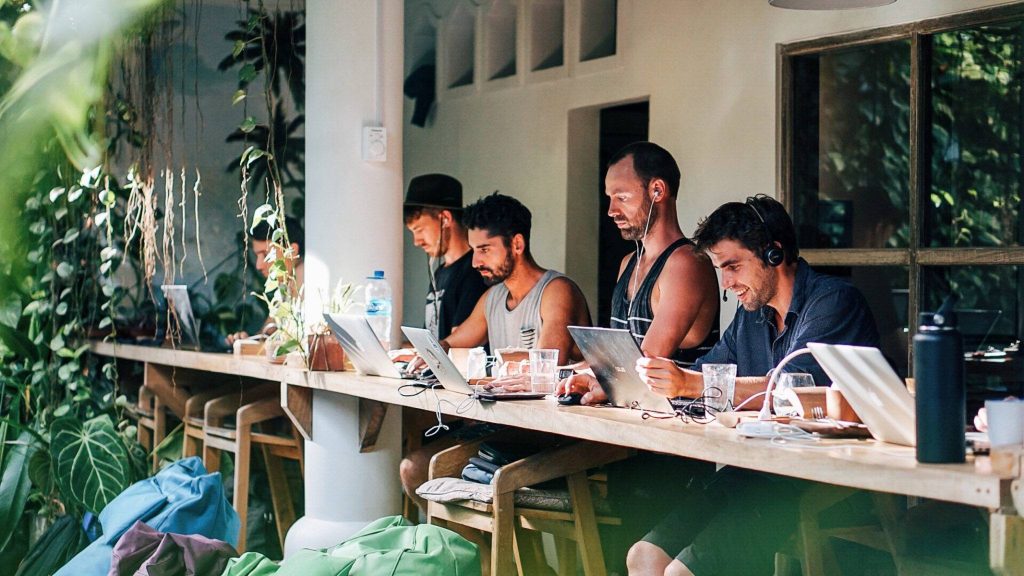 a group of men sitting at a long table with laptops