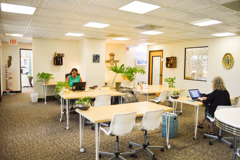 a woman sitting at a desk in a room with white chairs and laptops