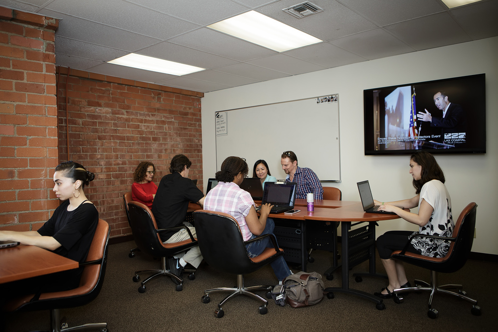 a group of people sitting around a table with laptops