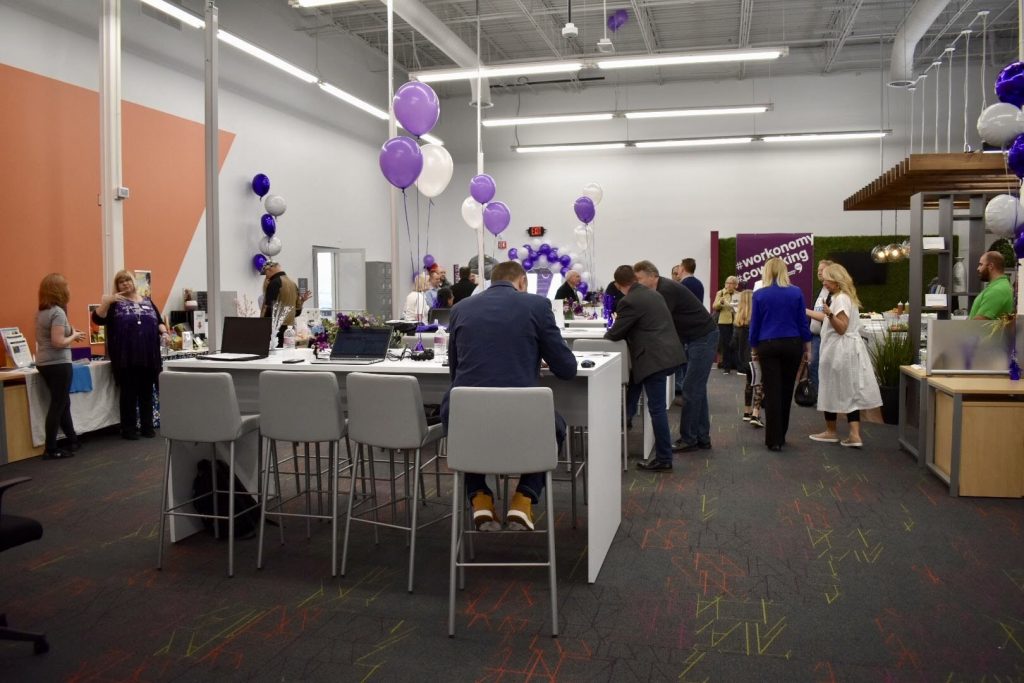 a group of people in a room with white tables and purple balloons