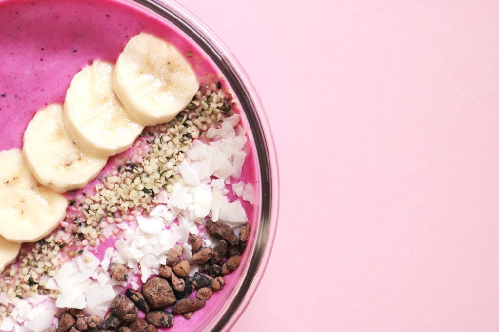 a bowl of pink smoothie with banana slices and nuts