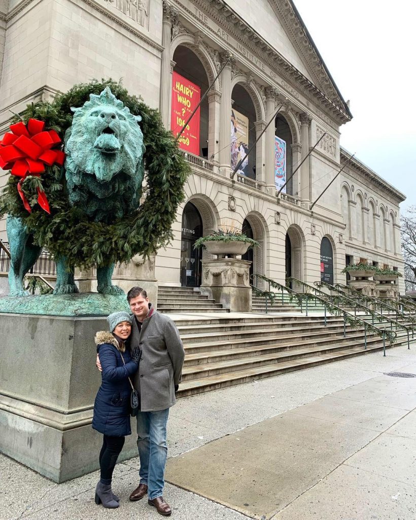 a man and woman standing in front of a statue of a lion with Art Institute of Chicago in the background