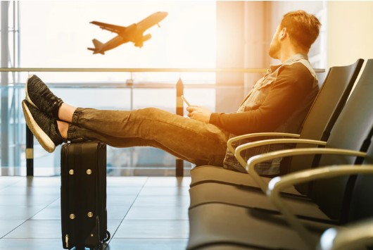 a man sitting in a airport lounge with his feet on his luggage