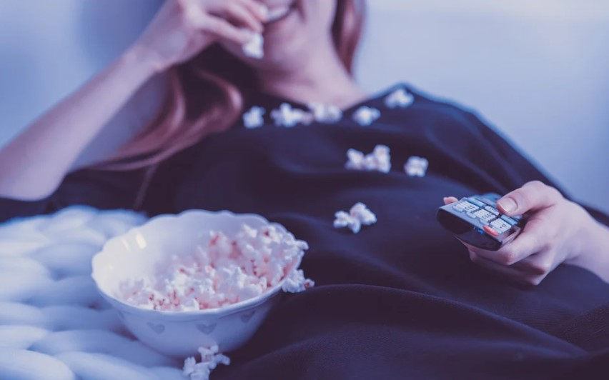 a woman lying down with popcorn and a bowl of popcorn