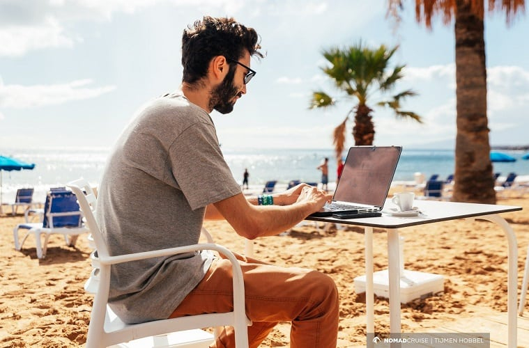 a man sitting at a table with a laptop on the beach